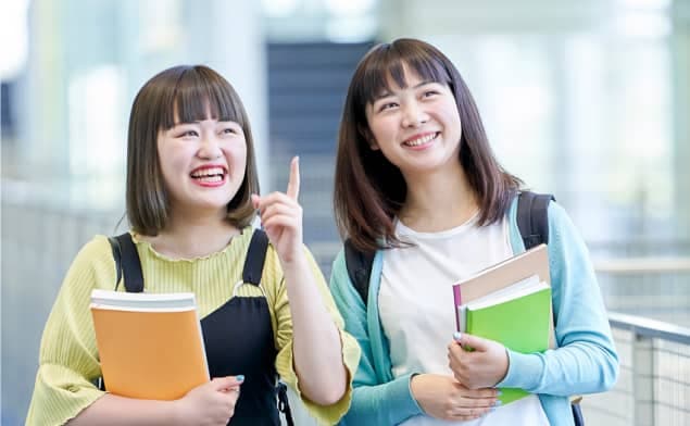 学校内で談笑をしながら歩く女性の大学生二人の写真