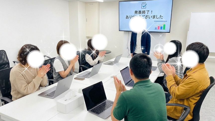 机の前で発表をしている利用者と、周りに座って拍手をしている利用者たちの画像