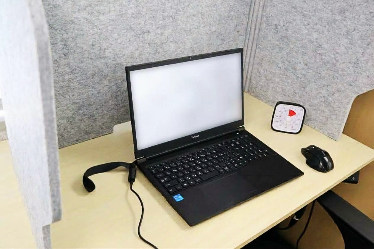 グレーのパーテーションで囲んだデスク。白い画面のノートPC、タイムタイマー、黒いマウスが置いてある。人の顔は写っていない